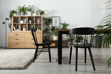 Photo of Table with chairs and wooden shelving unit, books and many potted houseplants in stylish room
