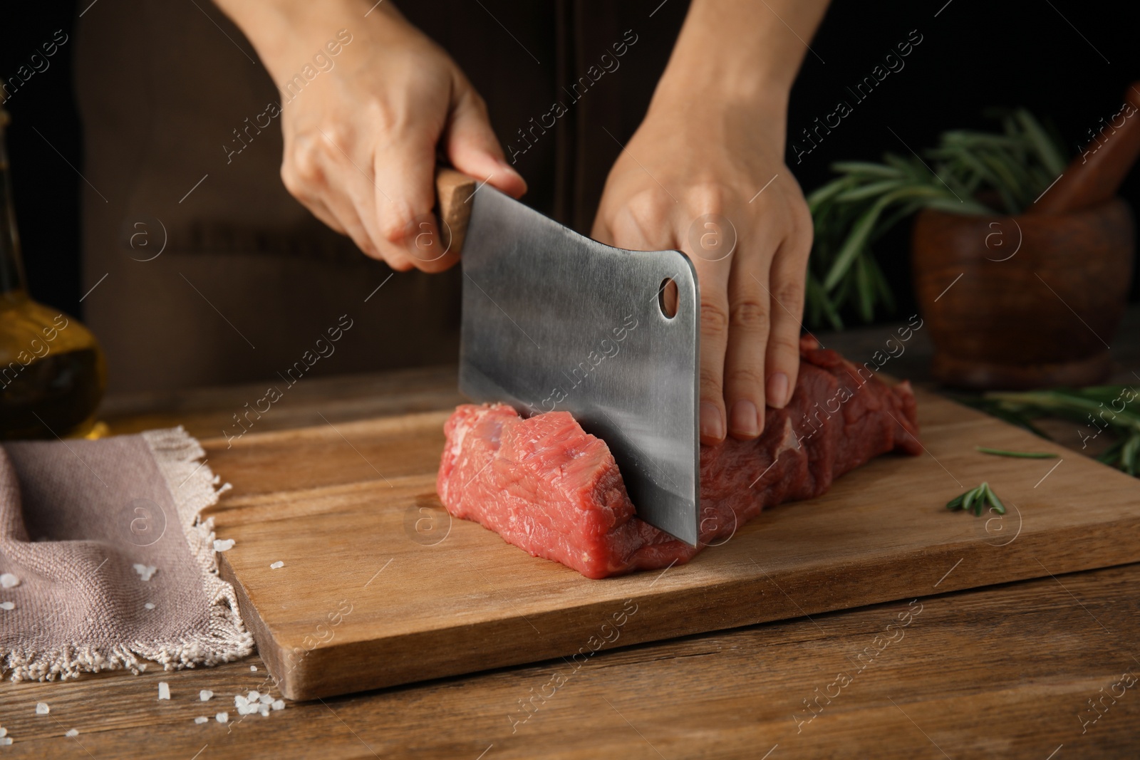 Photo of Woman cutting fresh raw meat at wooden table, closeup