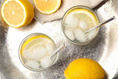 Photo of Soda water with lemon slices and ice cubes on silver tray, flat lay