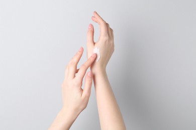 Woman applying cream on her hand against grey background, closeup