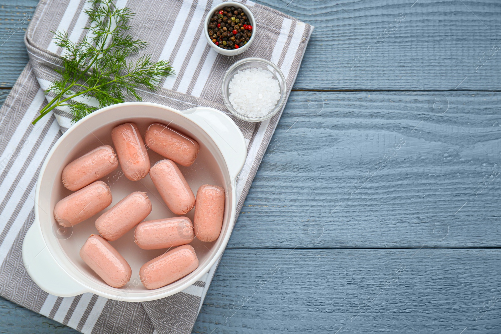 Photo of Bowl of delicious sausages, dill, salt and pepper on grey wooden table, flat lay. Space for text