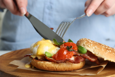 Woman eating tasty egg Benedict at table, closeup