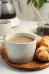 Aromatic coffee in cup and tasty profiteroles on white wooden table