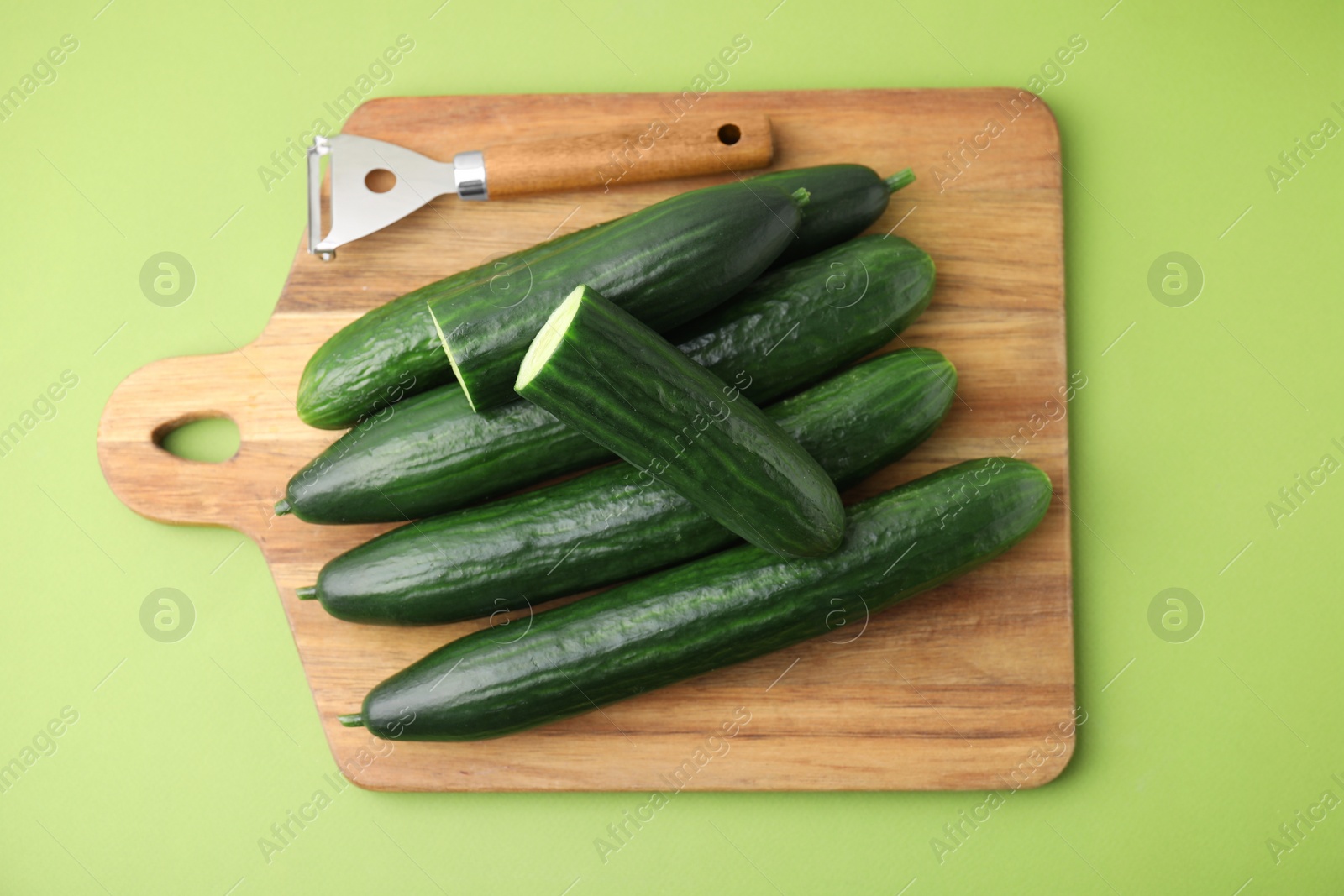 Photo of Fresh cucumbers and peeler on green background, top view