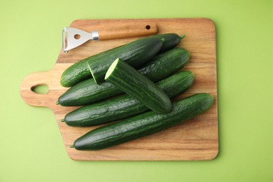 Fresh cucumbers and peeler on green background, top view