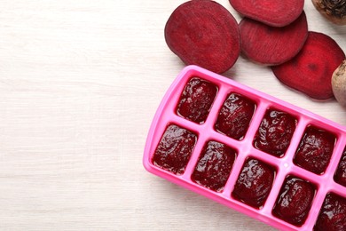 Photo of Beet puree in ice cube tray ready for freezing on white wooden table, flat lay. Space for text