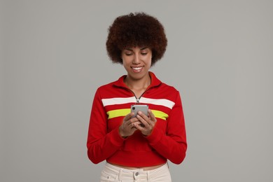 Happy young woman with smartphone on grey background