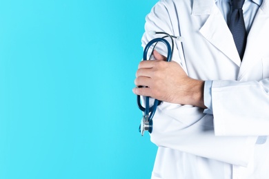 Photo of Male doctor holding stethoscope on color background, closeup with space for text