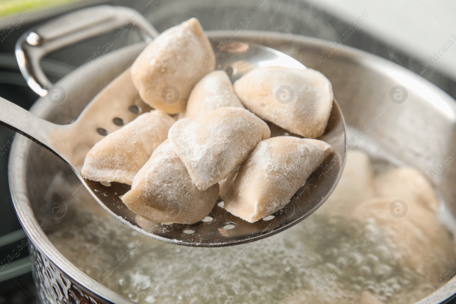 Photo of Closeup of dumplings on skimmer over stewpan with boiling water. Home cooking