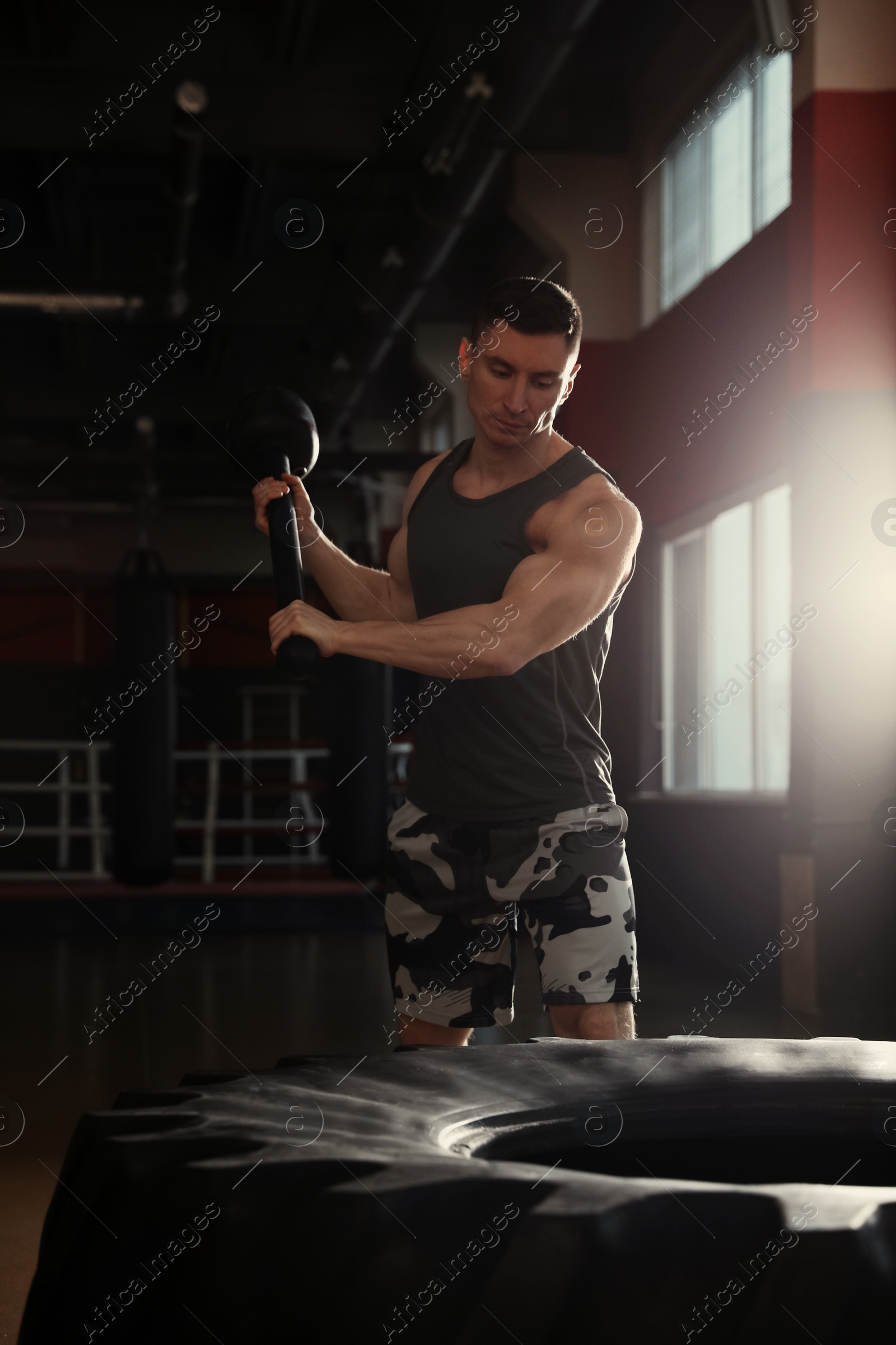 Photo of Strong man hitting heavy tire with hammer in gym