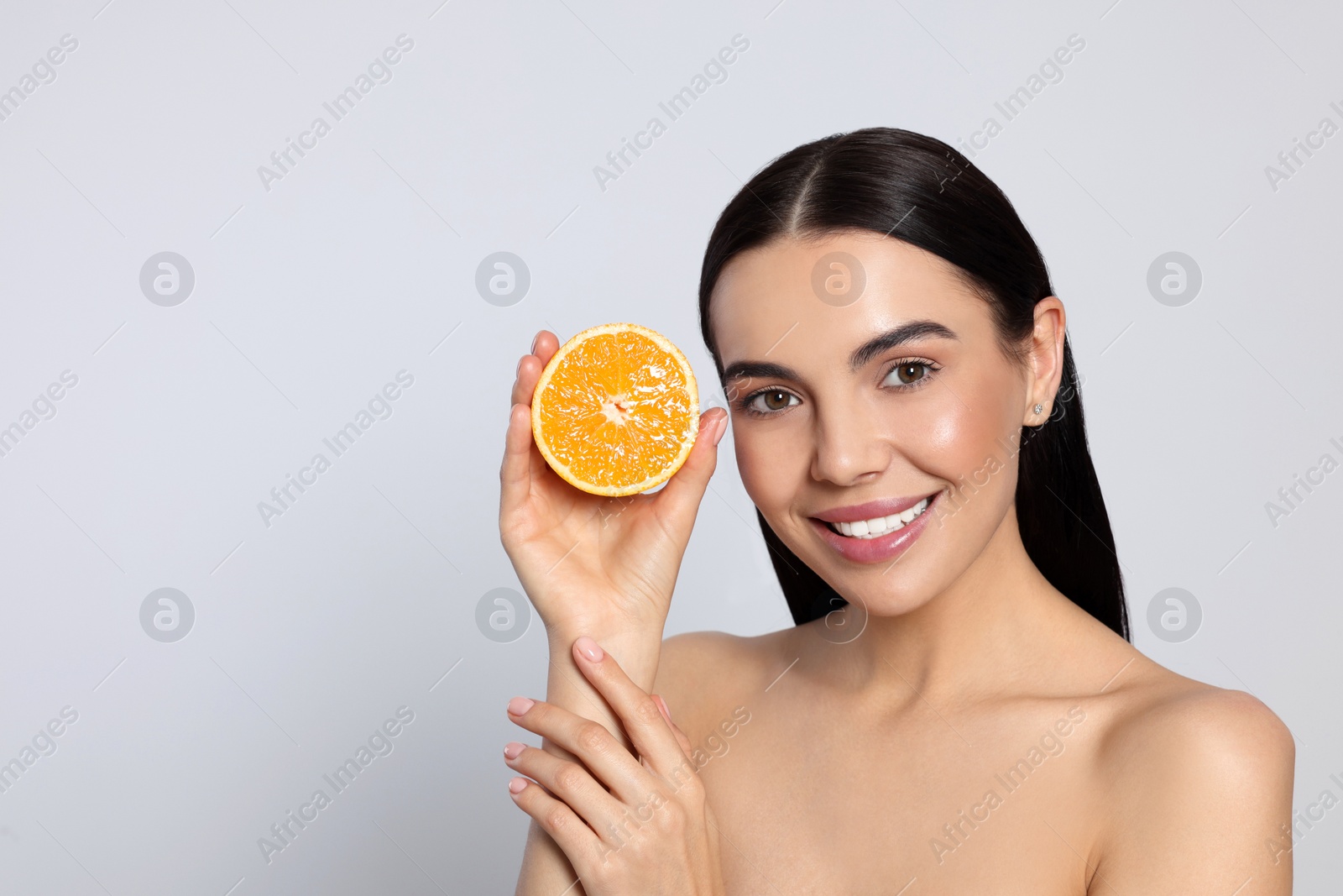 Photo of Woman holding half of orange on light grey background, space for text. Spa treatment