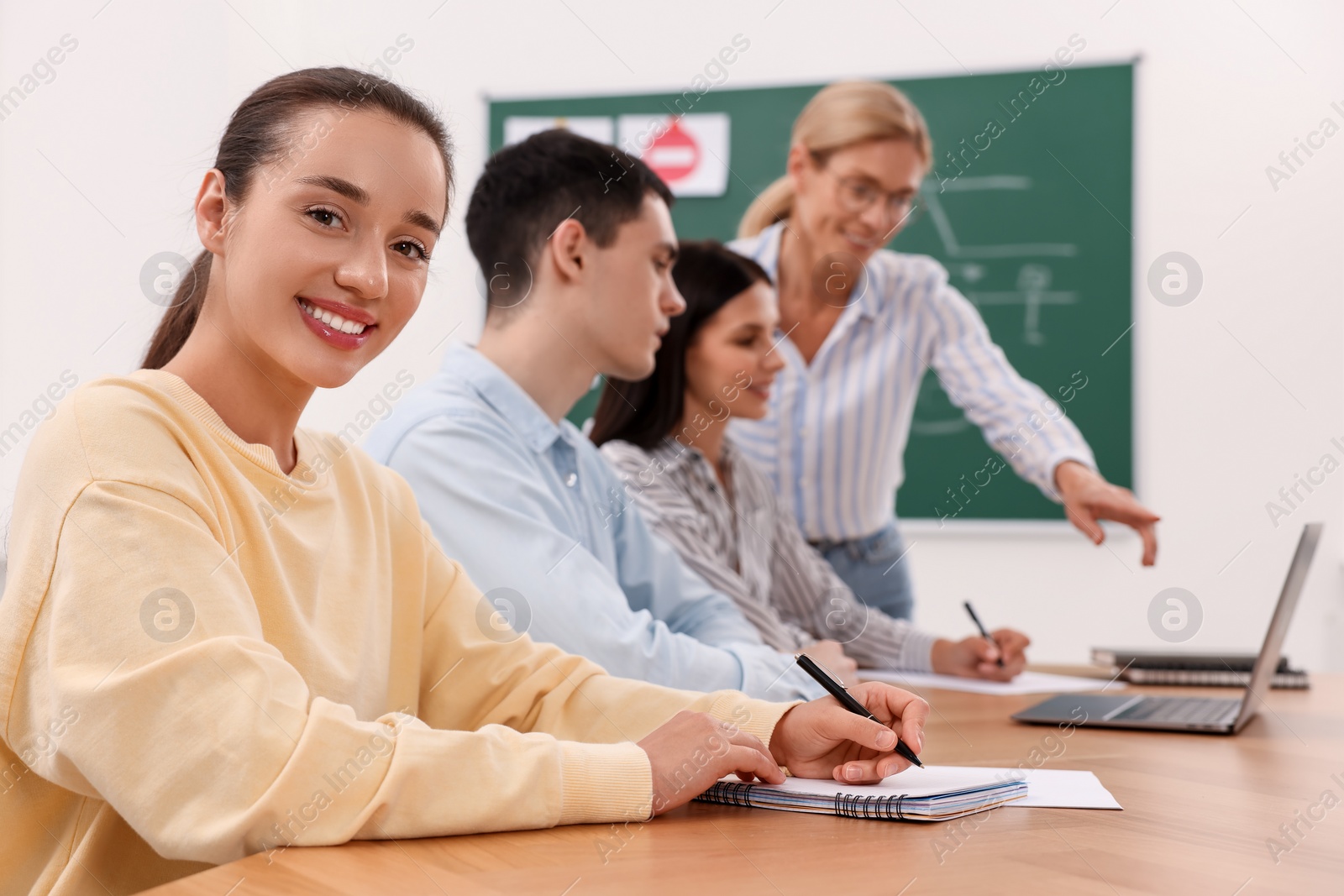 Photo of Happy woman making notes at desk in class during lesson in driving school