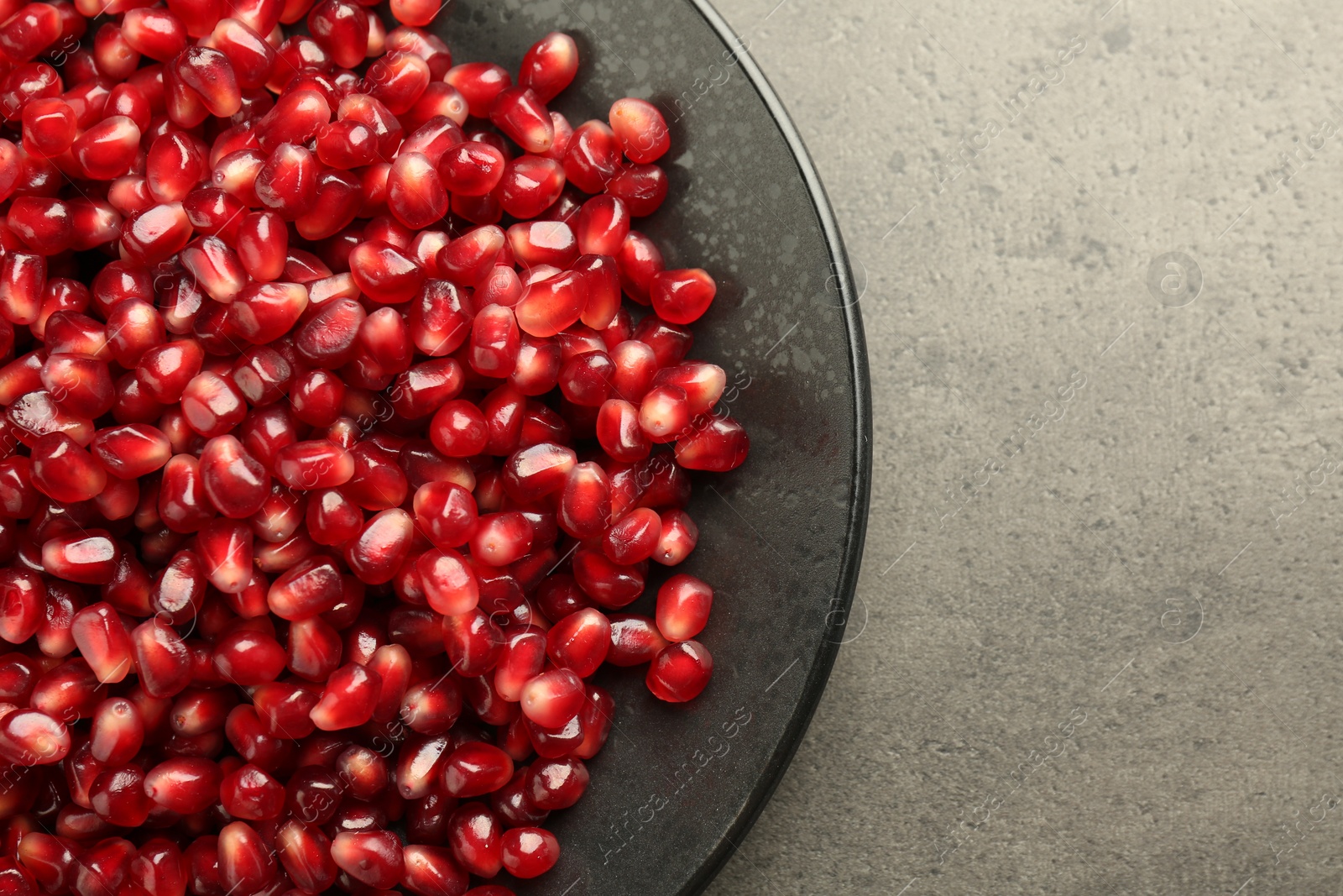 Photo of Ripe juicy pomegranate grains on grey textured table, top view. Space for text