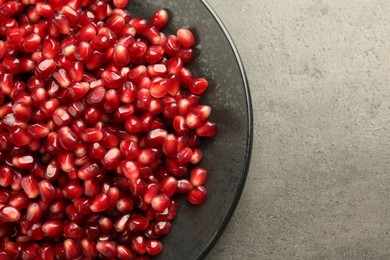 Photo of Ripe juicy pomegranate grains on grey textured table, top view. Space for text