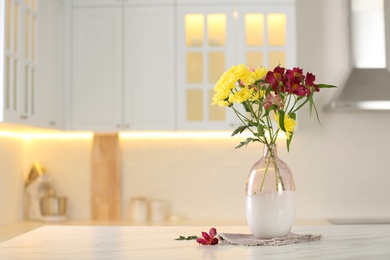 Photo of Vase with beautiful flowers on table in kitchen, space for text. Stylish element of interior design