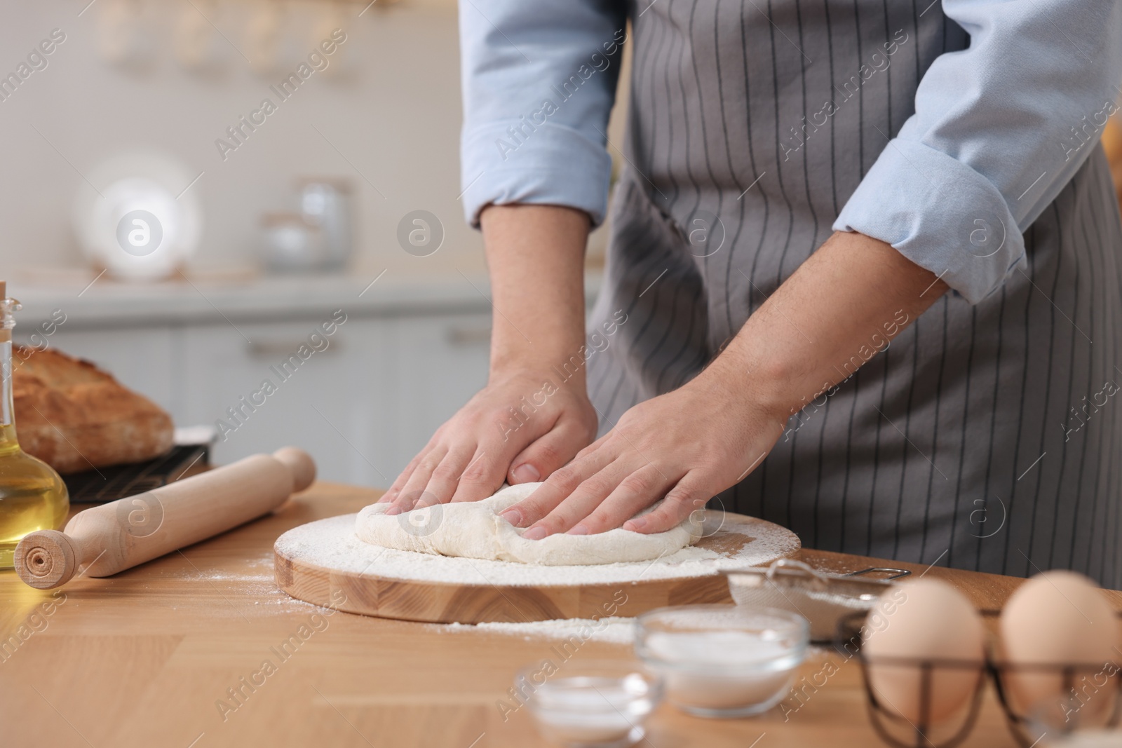 Photo of Making bread. Man kneading dough at wooden table in kitchen, closeup