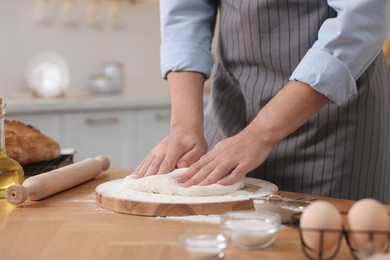 Making bread. Man kneading dough at wooden table in kitchen, closeup