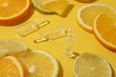 Skincare ampoules with vitamin C and citrus slices on yellow background, closeup