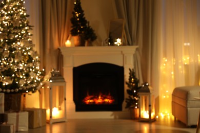 Photo of Beautiful fireplace, Christmas tree and other decorations in living room at night, blurred view. Interior design