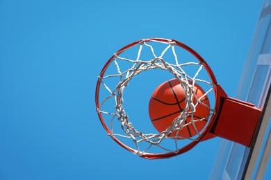 Basketball ball and hoop with net outdoors on sunny day, bottom view