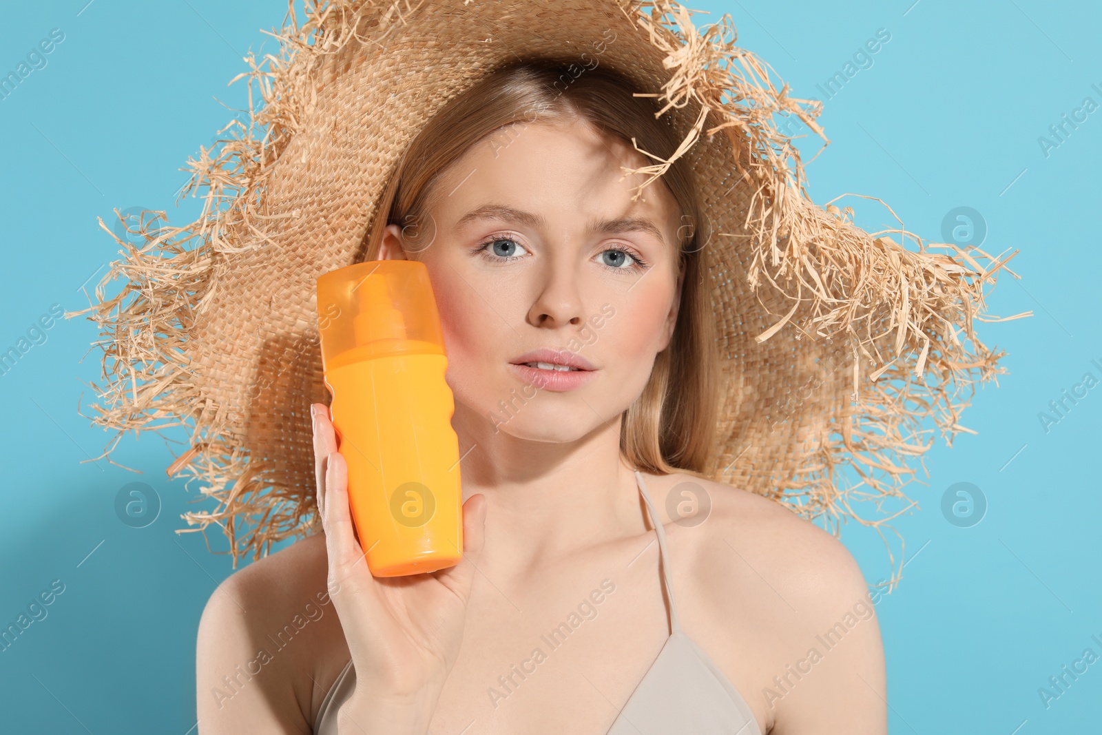 Photo of Beautiful young woman in straw hat with sun protection cream on light blue background