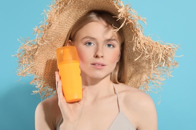 Beautiful young woman in straw hat with sun protection cream on light blue background