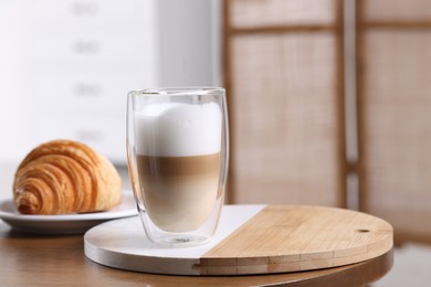 Photo of Aromatic latte macchiato in glass and croissant on wooden table against blurred background. Space for text