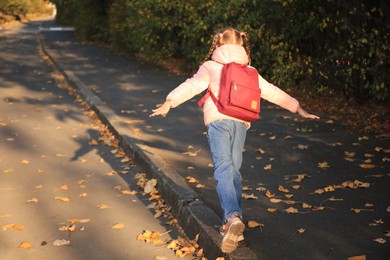 Photo of Cute little girl with backpack on city street, back view. Space for text