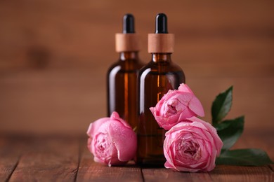 Photo of Bottles of essential rose oil and flowers on wooden table