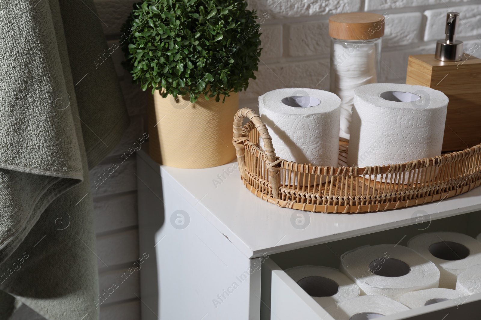 Photo of Toilet paper rolls, floral decor, dispenser and cotton pads on chest of drawers indoors