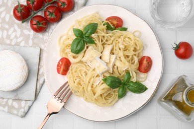 Delicious pasta with brie cheese, tomatoes and basil leaves served on white tiled table, flat lay