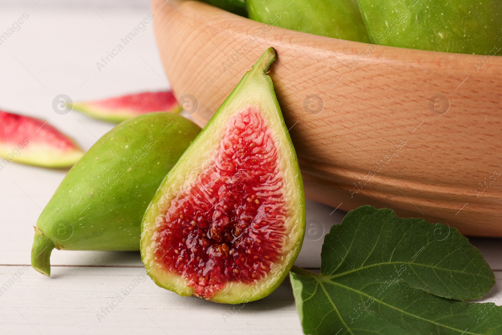 Photo of Cut and whole fresh green figs on white wooden table, closeup