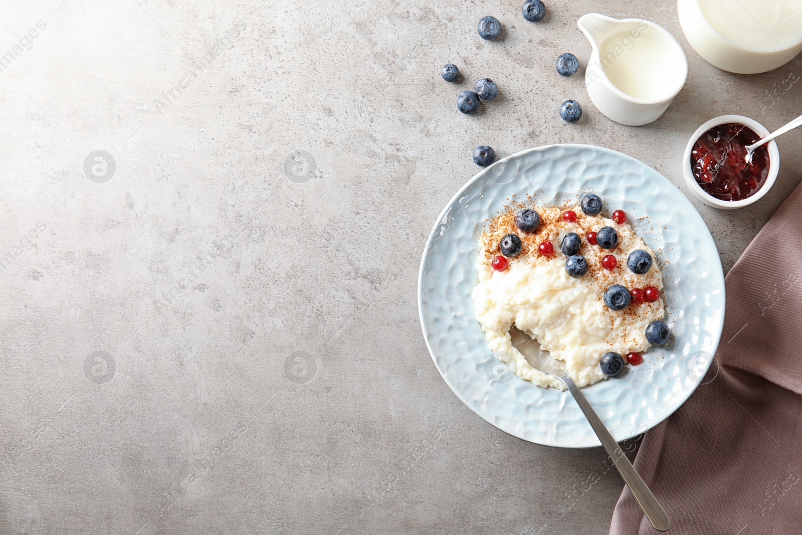 Photo of Creamy rice pudding with red currant and blueberries in bowl served on grey table, top view. Space for text