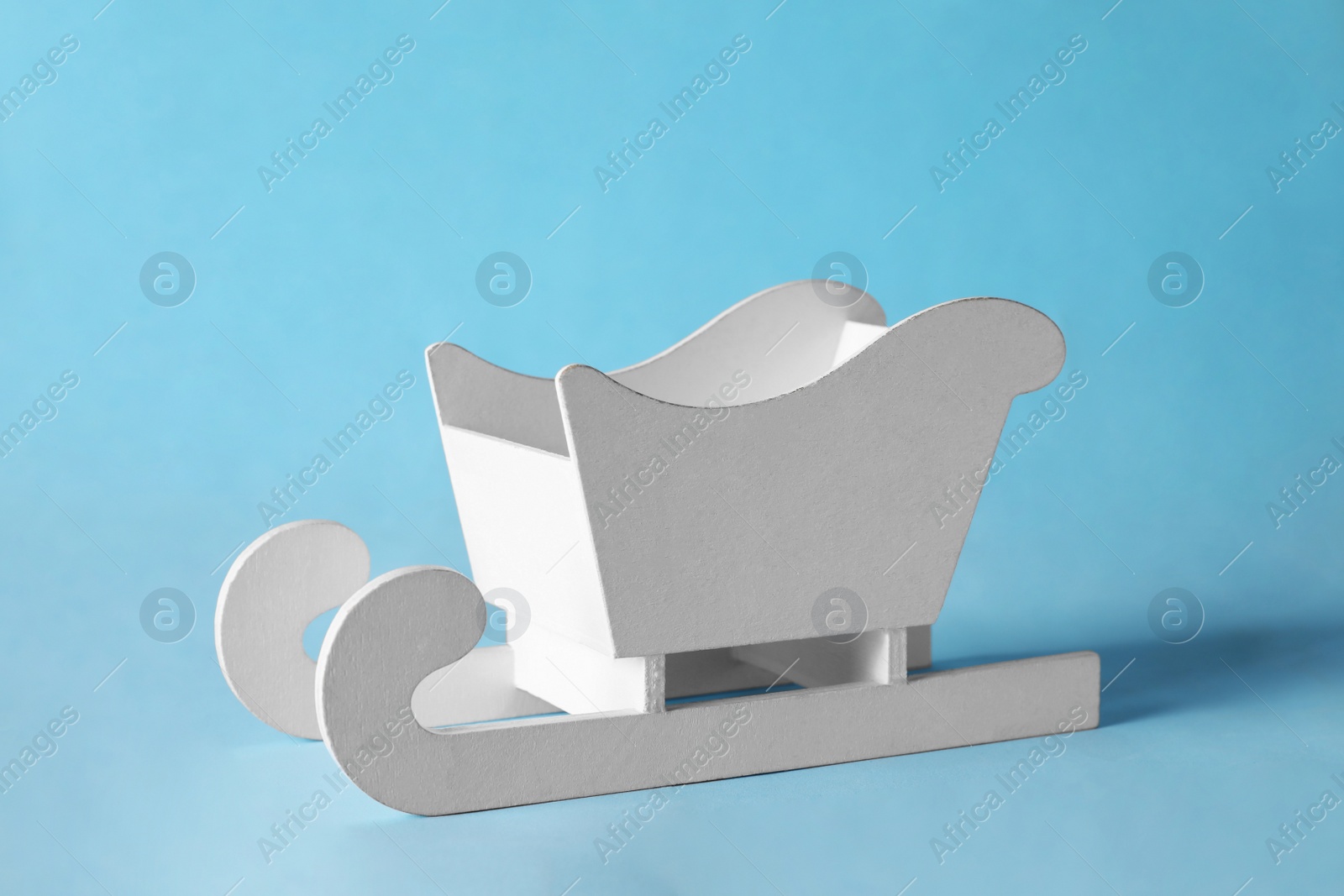 Photo of Decorative white wooden sleigh on light blue  background