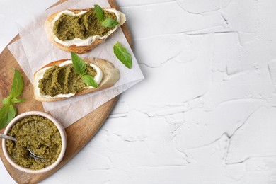 Photo of Tasty bruschettas with cream cheese, pesto sauce and fresh basil on white textured table, top view. Space for text