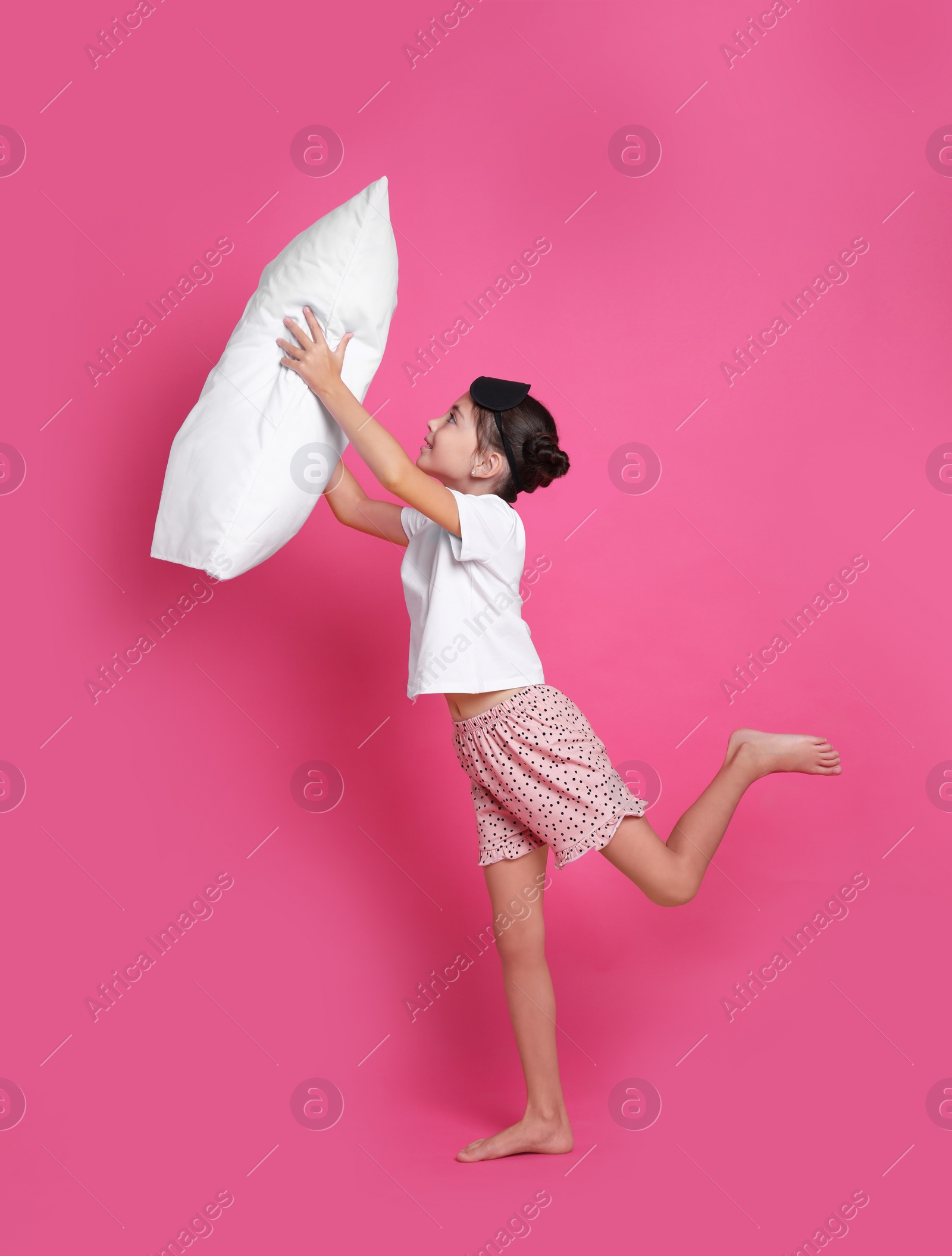 Photo of Cute girl in pajamas with pillow on pink background