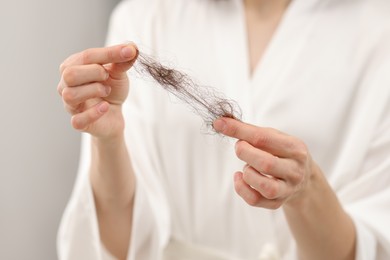 Photo of Woman holding lost hair on light background, closeup. Alopecia problem