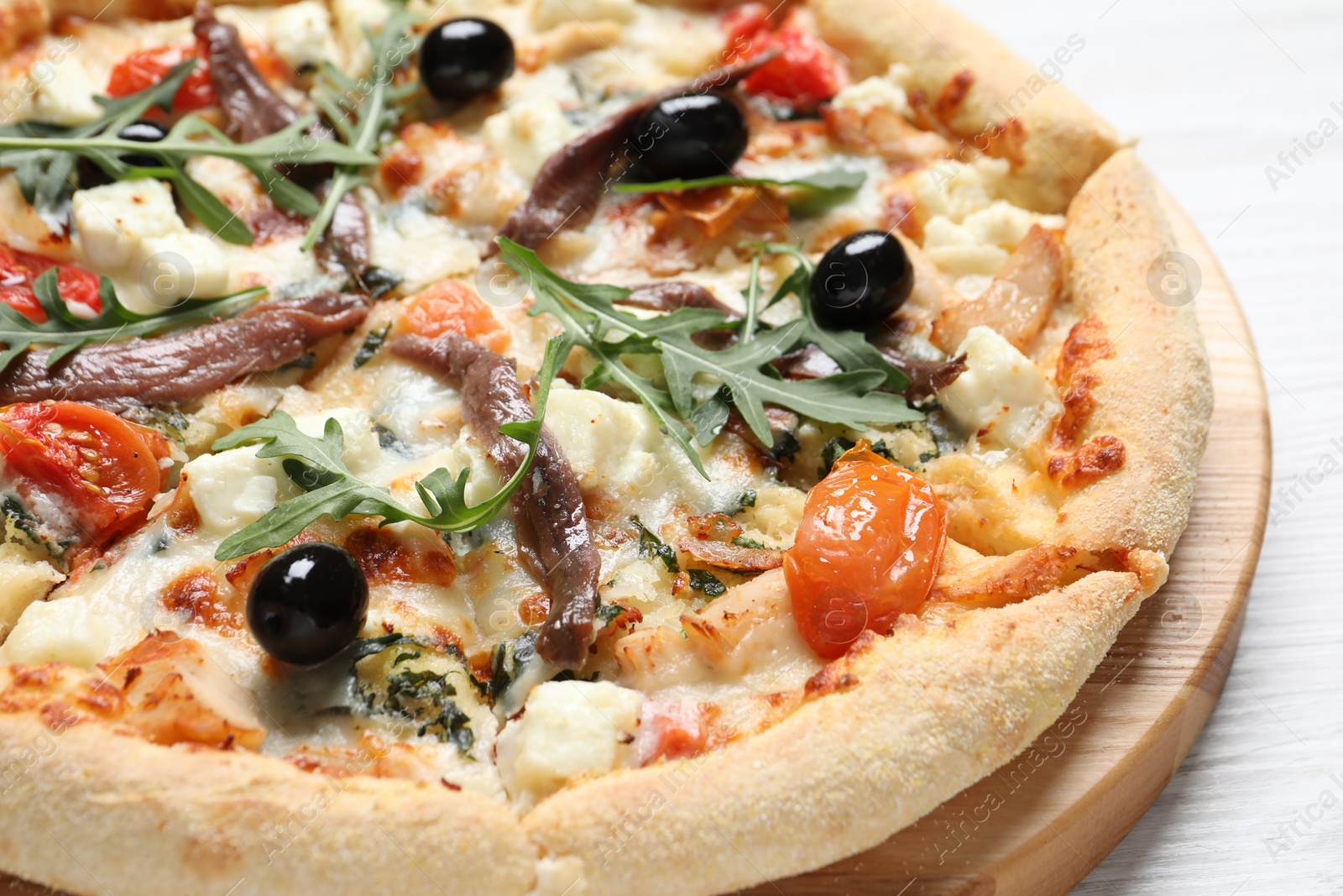 Photo of Tasty pizza with anchovies, arugula and olives on white wooden table, closeup