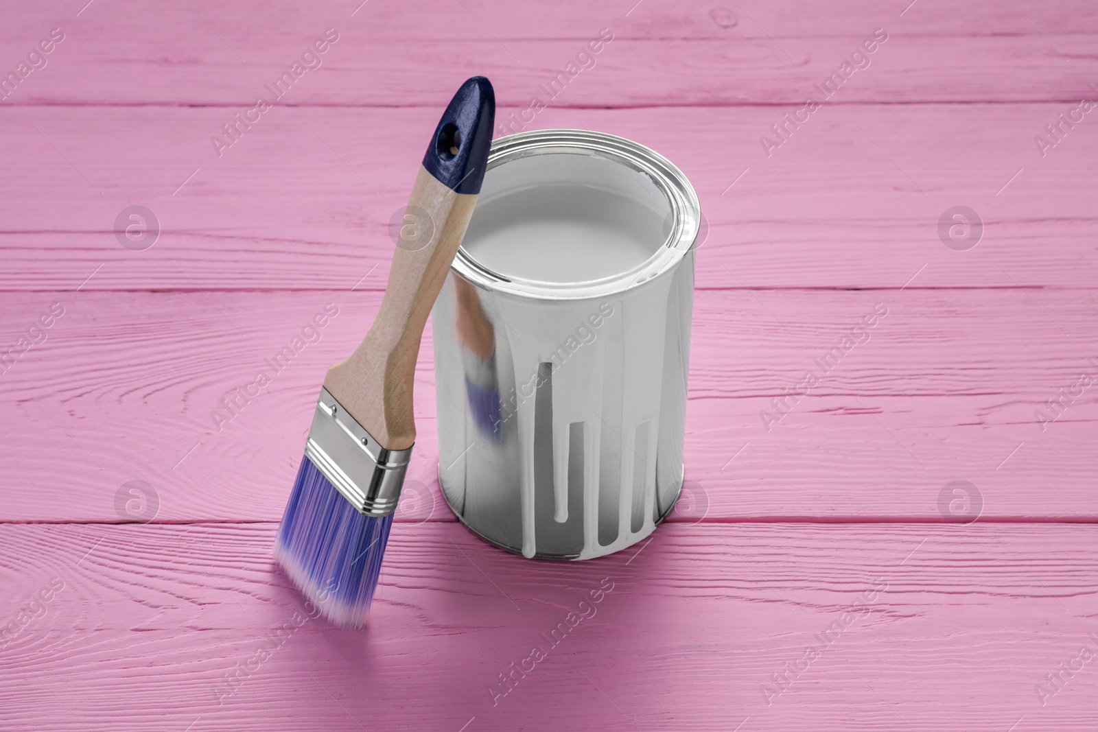 Photo of Can of white paint and brush on pink wooden table