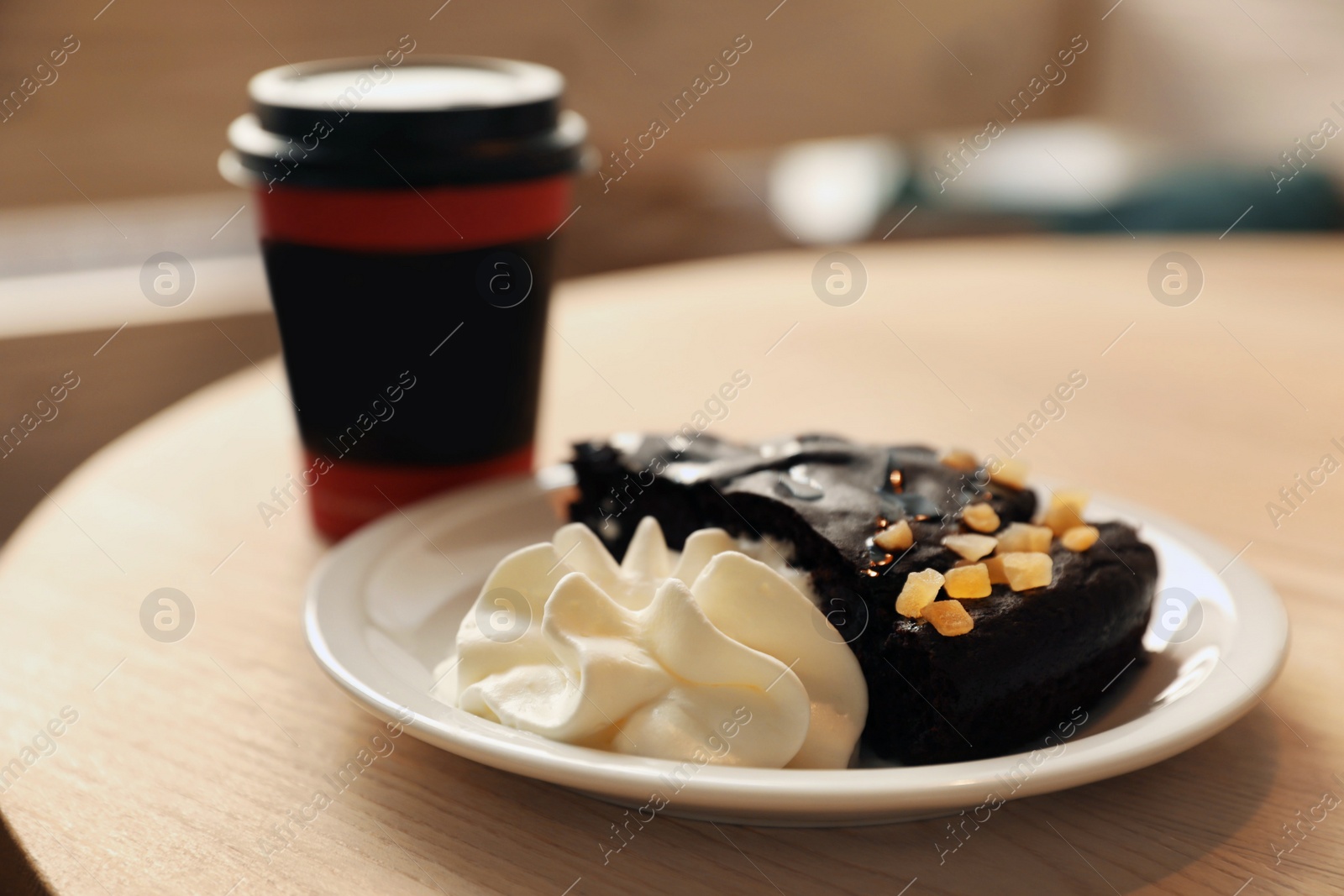 Photo of Tasty coffee in takeaway paper cup and dessert on wooden table at cafe, closeup