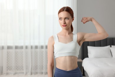 Photo of Woman in sportswear showing muscles in bedroom, space for text