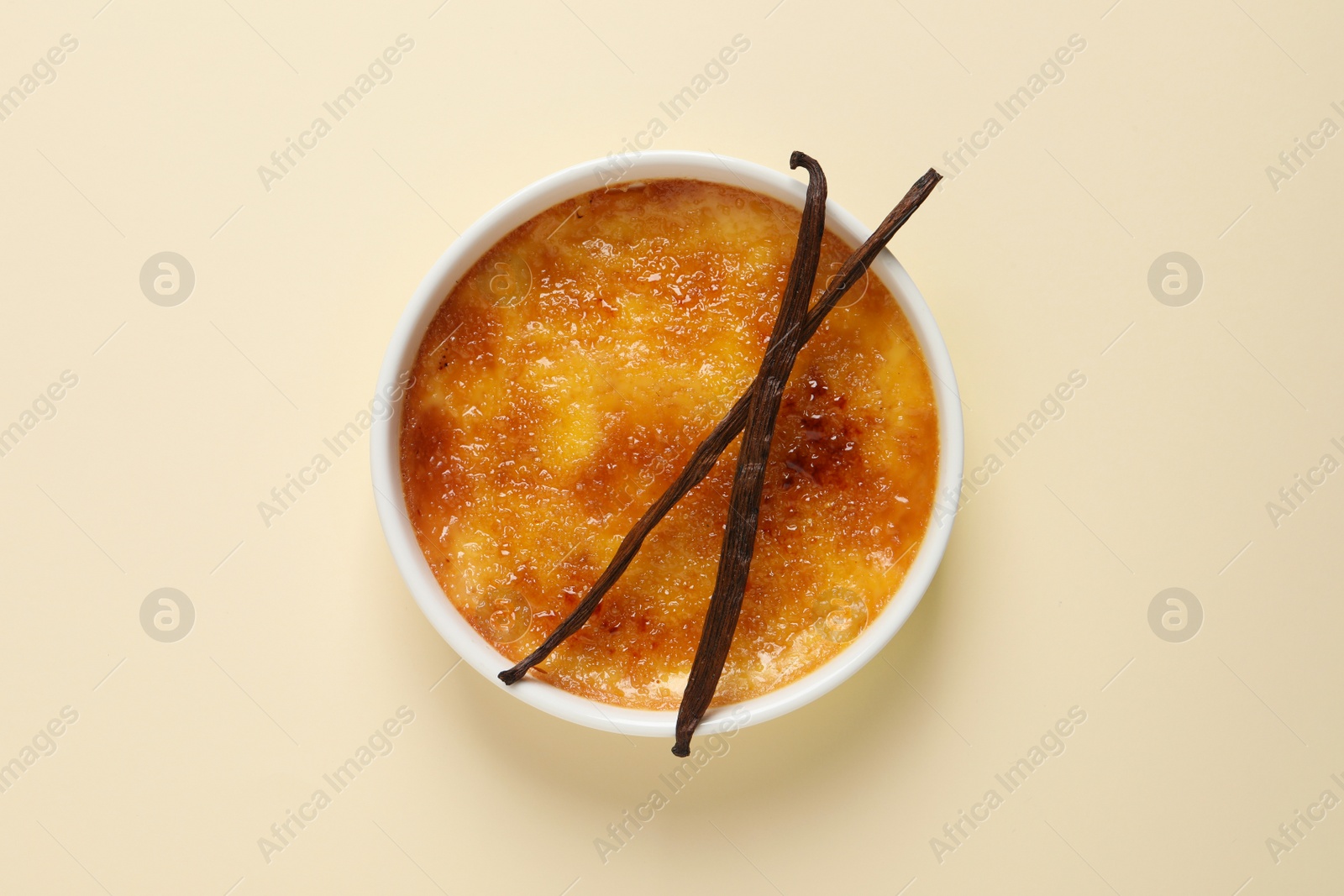 Photo of Delicious creme brulee with vanilla sticks on beige background, top view