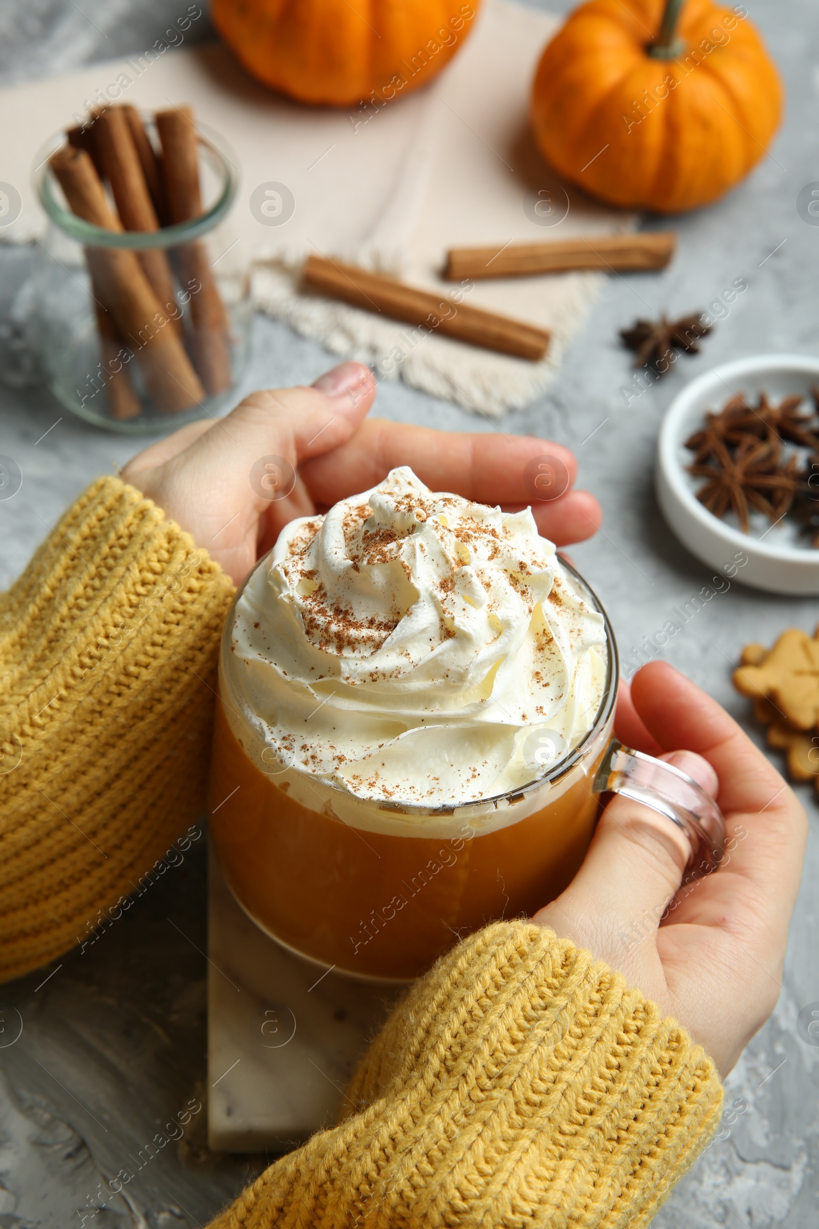 Photo of Woman holding cup of pumpkin spice latte with whipped cream at light grey table, closeup