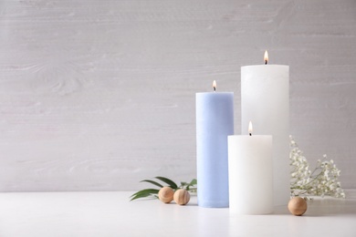 Pillar wax candles burning on table against light background