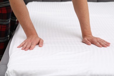 Photo of Man touching soft mattress with bed sheet, closeup
