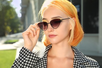 Beautiful young woman with bright dyed hair in sunglasses outdoors