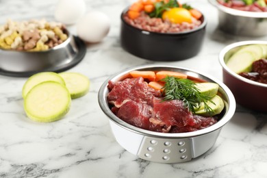 Photo of Natural pet food in feeding bowls on white marble table, closeup