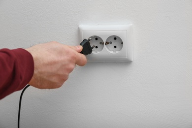 Photo of Electrician inserting plug into power socket on white background, closeup