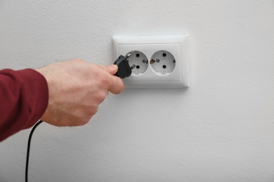 Electrician inserting plug into power socket on white background, closeup