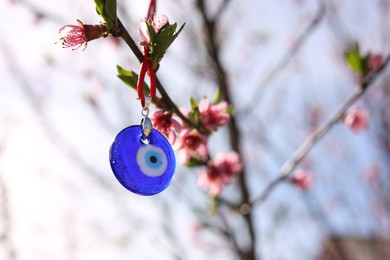 Evil eye amulet hanging on blossoming spring tree outdoors. Space for text